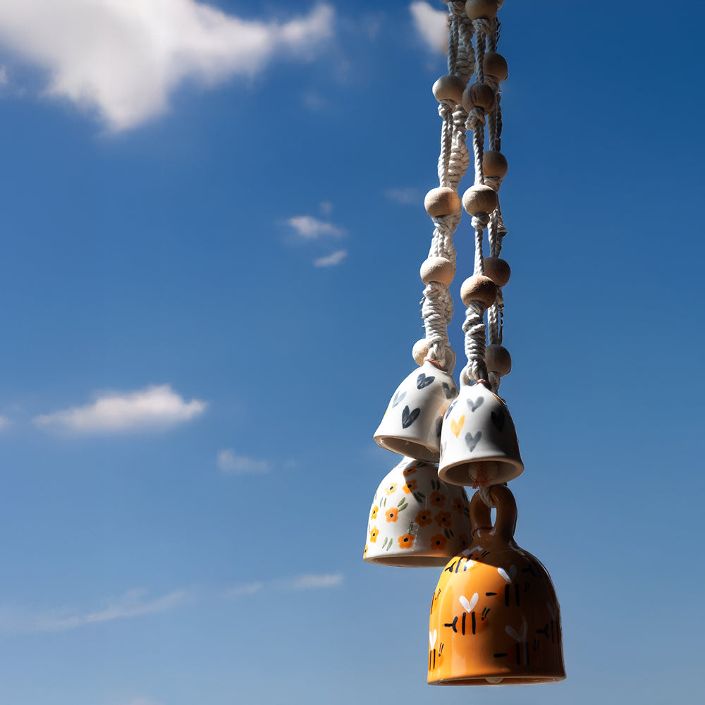 Decorative ceramic bells hanging against a blue sky with clouds