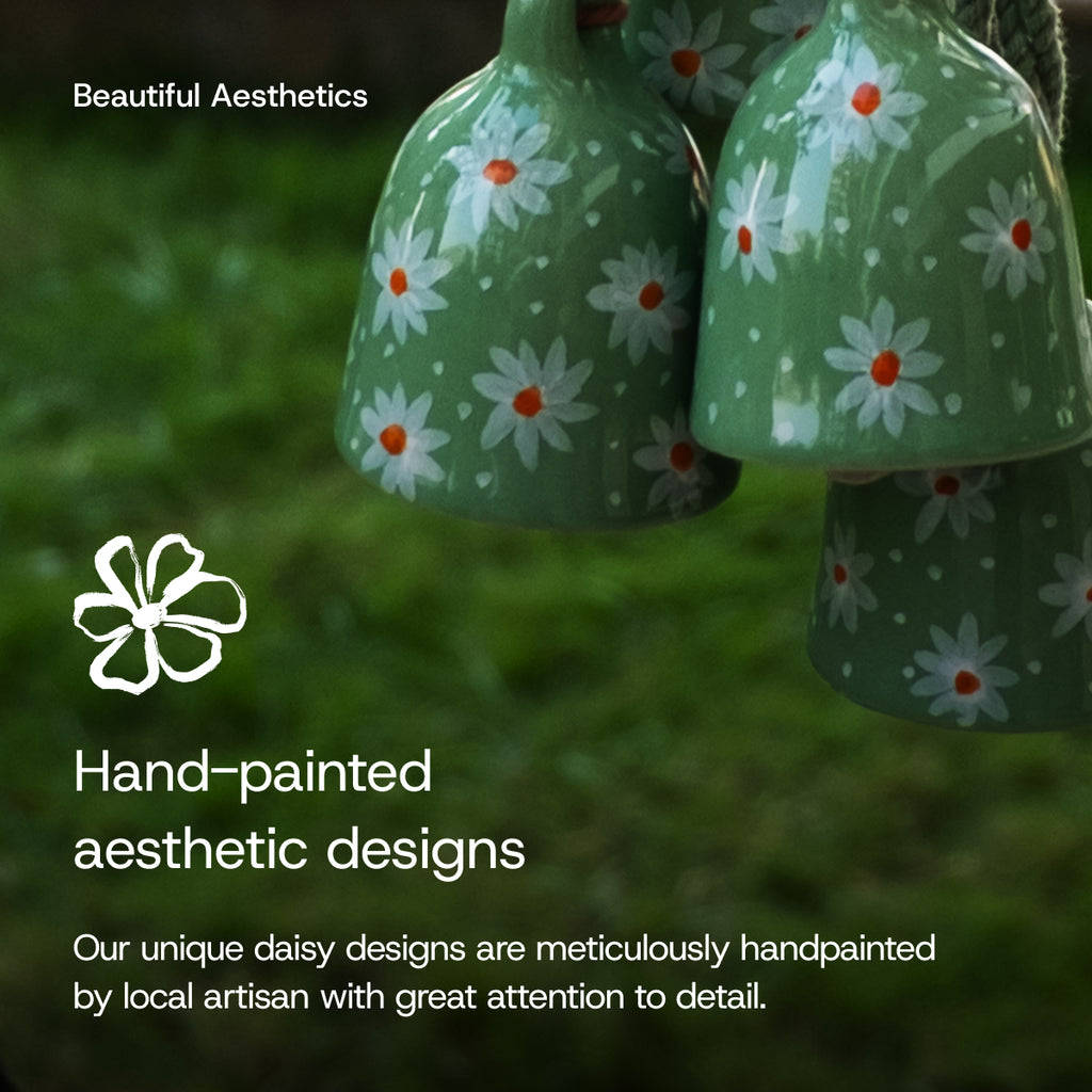 Hand-painted green ceramic bells with daisy designs on a grassy background