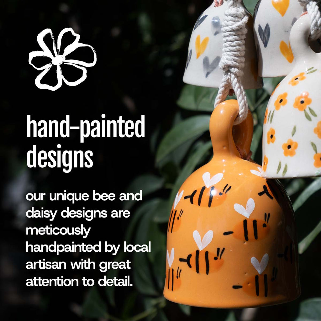 Hand-painted ceramic bells with bee and daisy designs on a dark background